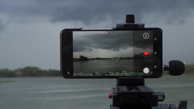 view of android smart phone recording VDO4K and shooting timelapse with rain storm anc dark clouds moving show on monitor, Krajub reservoir, Banpong, Ratchaburi, Thailand.