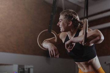 Happy healthy athletic woman laughing, looking away, resting after gymnastic rings workout. Cheerful crossfit female athlete relaxing at the gym, after exercising