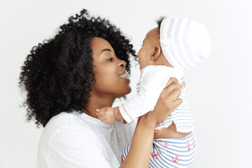 Closeup portrait of beautiful african woman holding on hands her little daughter on white background. Family, love, lifestyle, motherhood and tender moments concepts. Mother's day concept or