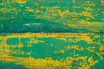 Old wooden painted rustic wall with yellow green flaky dye. Faded wood plank close-up. Peeling paint on board. Damaged rough wooden texture. Imperfect wood surface. Background with weathered paint.