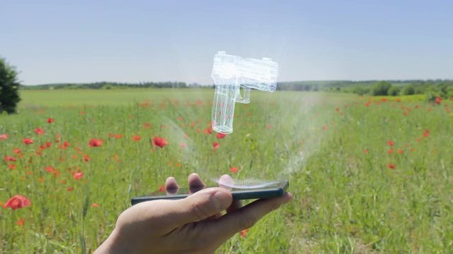 Hologram of gun on a smartphone. Person activates holographic image on the phone screen on the field with blooming poppies