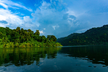 Landscape of mountains and water with reflection in Khun Dan Prakarnchon Dam in cloudy blue sky day at Nakhon Nayok, Thailand