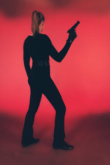 Fototapeta na wymiar Silhouette of woman in black holding pistol. Against red background.