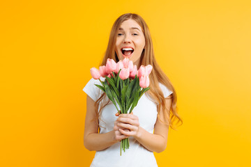 Happy girl , holding a bouquet of flowers in her hand, delighted with the gift on a yellow background