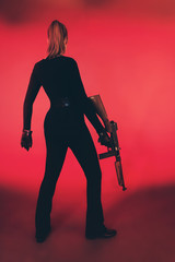 Young woman standing with machine gun against red background.