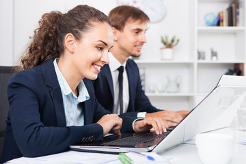 Glad business female assistant wearing formalwear using laptop