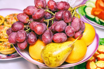 Bunch of grapes, pear and orange on the plate