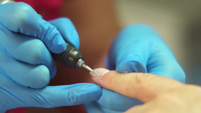 Polishing (buffing) nails with an electric nail file. Close-up of manicurist hands in disposable, blue gloves filing the client&rsquo;s nail 