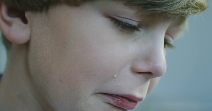 Close up of the face of teen blond Caucasian boy crying and being very upset. Indoor. Portrait.