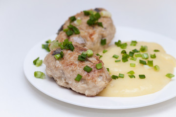 Delicious fried homemade fish cakes or cutlets on white plate with green onion and potato.