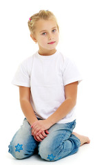 A little girl is sitting on the floor in a clean white T-shirt.