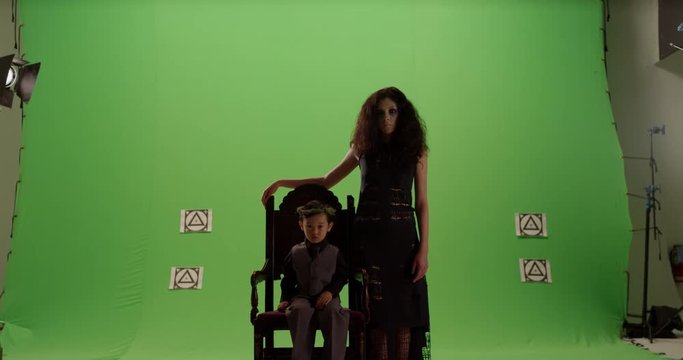 Mysterious little boy child sitting on old antique chair throne with woman beside him abstract against green screen in slow motion