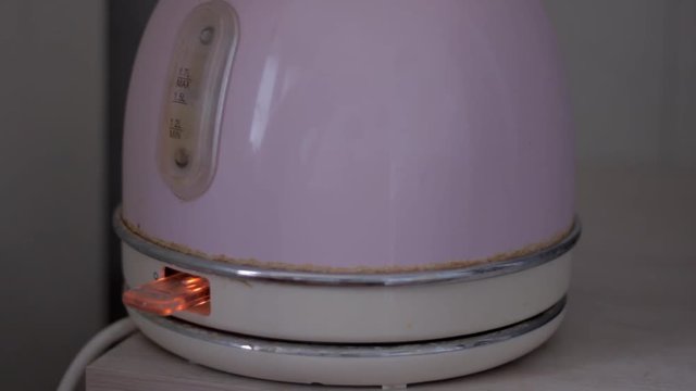 Turning on by pressing  button the old electric kettle with water on table. Boiling and turning off the kettle
