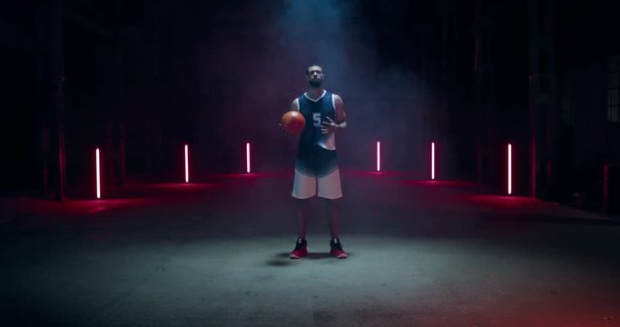 WIDE African American professional basketball player posing with a ball against dark background in a large abandoned warehouse. 4K UHD 60 FPS SLOW MOTION