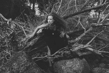 Curly hair woman in a black dress on the nature in the forest