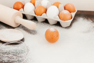 Flour on wooden desk, eggs, wooden kitchen utensils