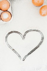 Heart of flour on wooden desk, eggs, kitchenware