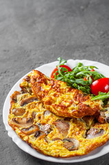 omelette with mushrooms and arugula salad in white plate on Dark grey black slate background