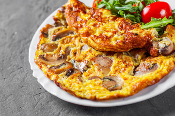 omelette with mushrooms and arugula salad in white plate on Dark grey black slate background