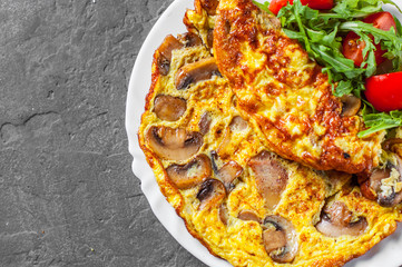 omelette with mushrooms and arugula salad in white plate on Dark grey black slate background