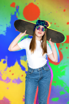 Teenager girl in sunglasses and hipster millennial hat with skateboard near the colorful wall, generation leisure concept