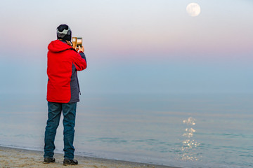 Frau macht Fotos mit dem Smartphone vom Mond am Meer 