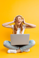 An image of a beautiful woman listening to music on headphones using a laptop while sitting...