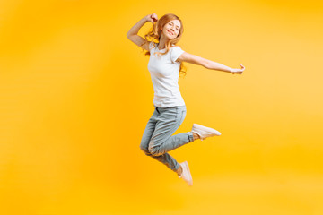 Portrait of a cheerful enthusiastic girl in a white T-shirt jumping for joy on a yellow background