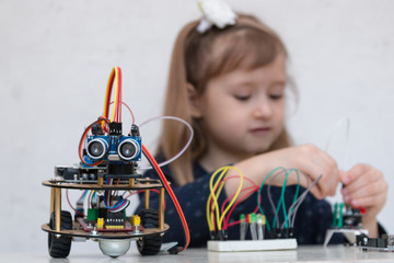 A cute girl constructs metal robot and program it. The boards and microcontrollers are on the...
