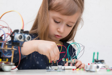 A cute girl constructs metal robot and program it. The boards and microcontrollers are on the table. STEM education inscription. Programming. Mathematics. The science. Technologie. DIY. 