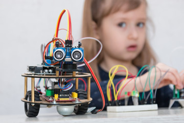 A cute girl constructs metal robot and program it. The boards and microcontrollers are on the table. STEM education inscription. Programming. Mathematics. The science. Technologie. DIY. 