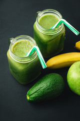 Green, healthy, detox smoothie from avocado, banana, apple in mason jar on dark background, vegetarian food