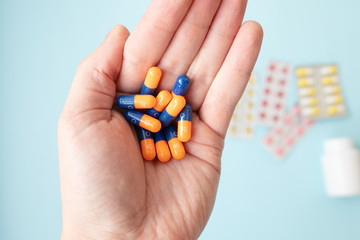 Close-up shot of a hand holding color pills on blue background.