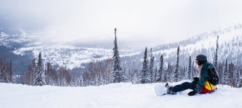 Panoramic picture of snowboarder sit in the mountains on a snowy slope.