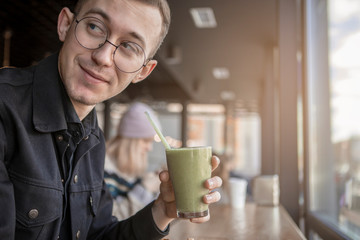 Young stylish man enjoys a cake and a drink while sitting in a cafe with large windows