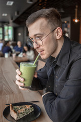 Handsome little bearded man holding smoothy and eating in cafe and smiling looking at camera