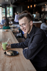 Side view of a smliling businessman talking on a phone while sitting in cafe, drink smoothy, eat pie