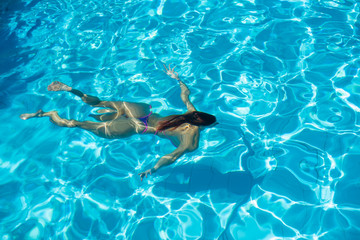 Obraz premium Over head rear view of an attractive young woman swimming under water and wearing in bikini