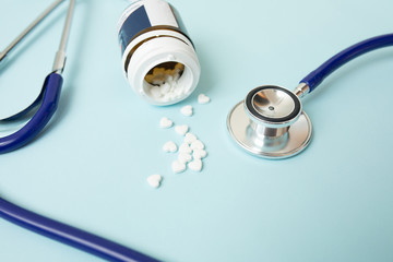 Pills in form of heart next to stethoscope on blue background. Medicine concept.