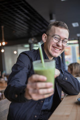 Young stylish man enjoys a cake and a drink while sitting in a cafe with large windows