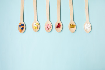 Variety of vitamin pills in wooden spoon on blue background. Healthcare concept. 