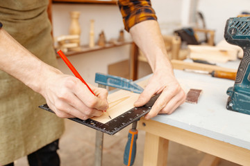 male carpenter measuring wooden blank with the lines and making marks with a pencil