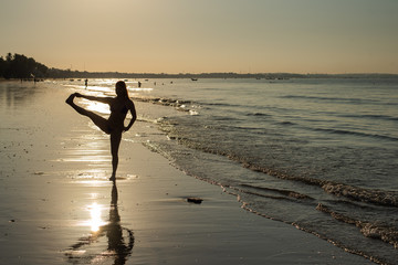 Fototapeta na wymiar Yoga silhouette at sunset on the sea shore. woman practices yoga and meditates on the beach