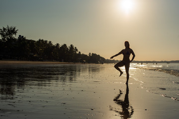 Yoga silhouette at sunset on the sea shore. woman practices yoga and meditates on the beach