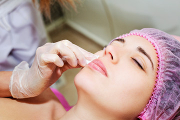 Depilation with hot wax mustache in the beauty salon. Young woman receiving facial epilation close up. Cosmetologist removes hair on face. Beauty salon, mustache depilation.