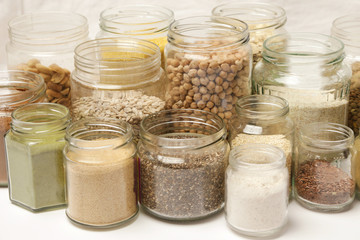 Many jars with grains, seeds, legumes, flours and various food ingredients. Healthy food concept.