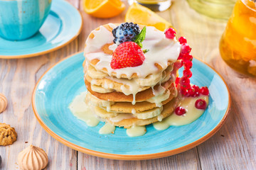 Stack of homemade pancakes with strawberrie, banana and red currant on a blue plate
