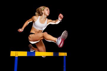 Sportswoman jumping over hurdle on sprint race