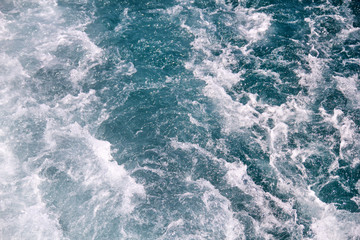 Turbulence made by foam of sea water from a high-speed yacht on surface of sea. Blue sea waves with lot of sea foam. Surface of sea with waves, splash, foam and bubbles, blue background and wallpaper.