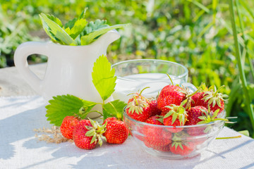 A bowl of strawberries, a jug and a cup of milk on a napkin on a wooden table